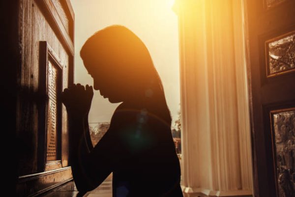 silhouette of woman kneeling and praying in modern church at sunset time